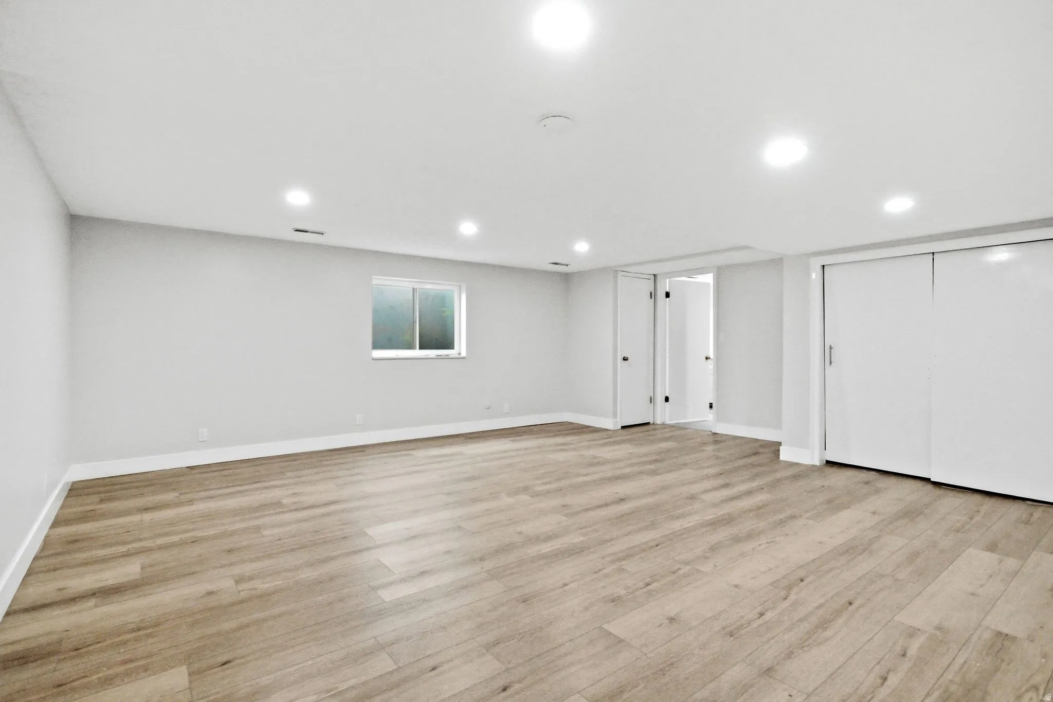 Spacious room featuring light wood-finish flooring, recessed lighting, and a neutral wall palette