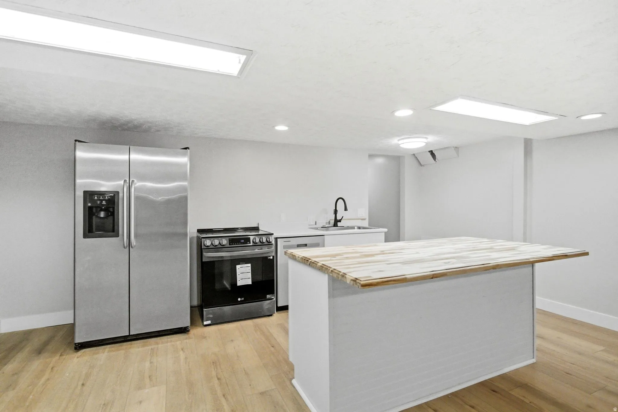 Open-concept kitchen area featuring a central island with a wood-finish countertop, white cabinetry, stainless steel appliances, and wood-finish flooring