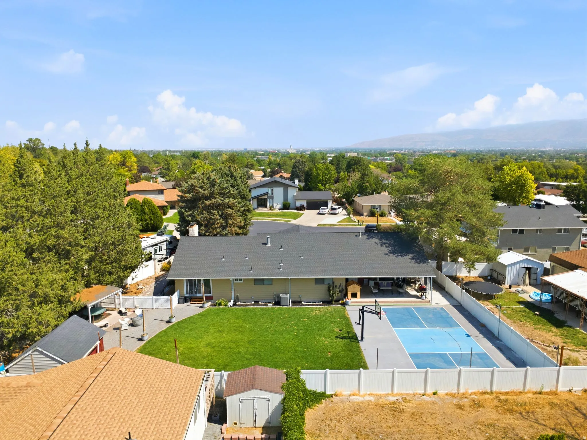 Expansive backyard featuring a large sports court with blue accents, a manicured green lawn, and a covered patio area