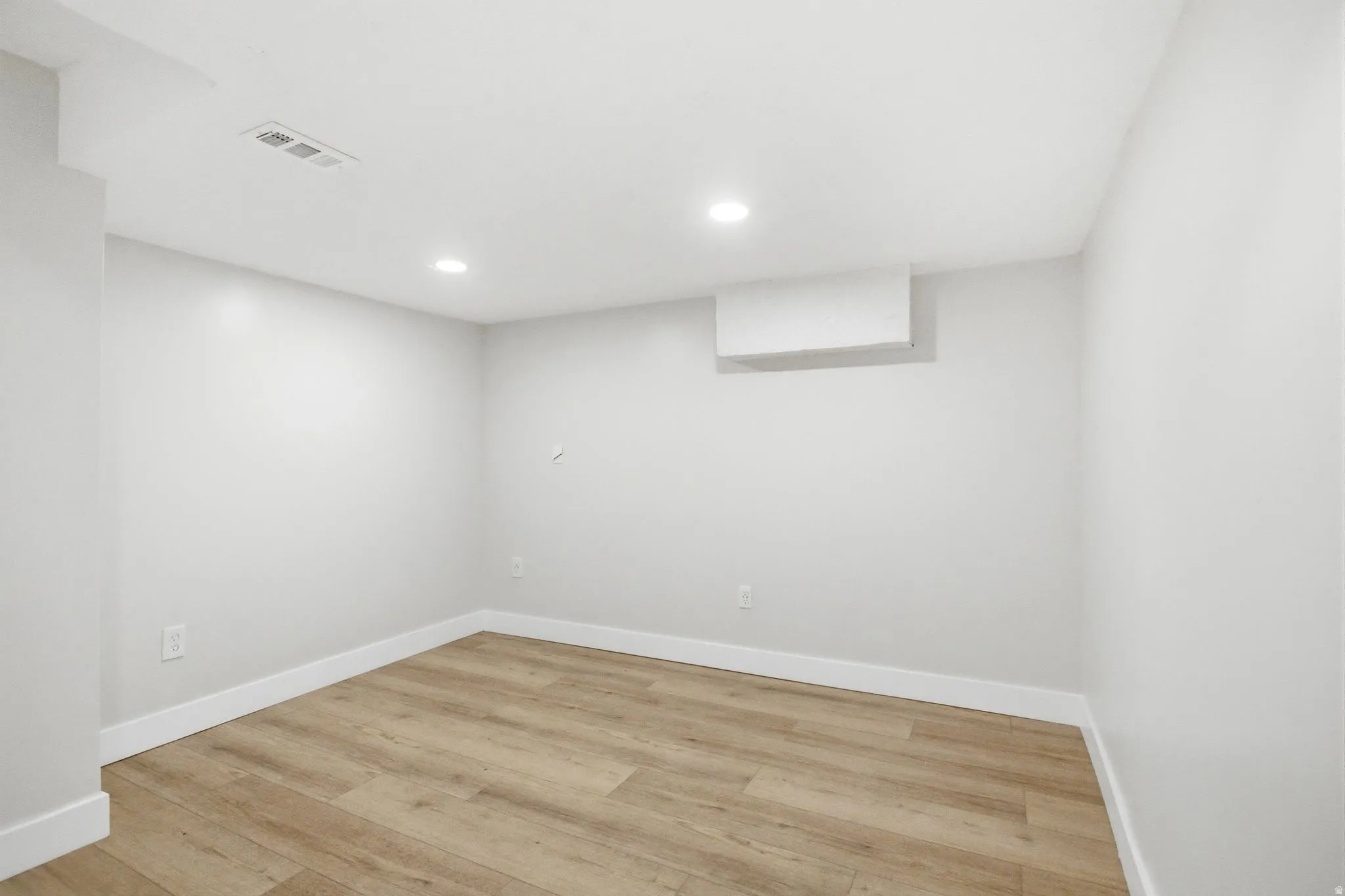 Spacious room with light wood-finish flooring, white baseboards, and neutral wall paint