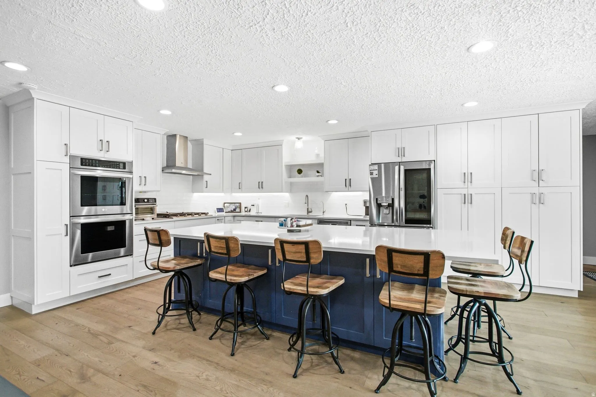 Spacious kitchen featuring an expansive center island, white cabinetry, stainless steel appliances, wood-finish flooring, and recessed lighting