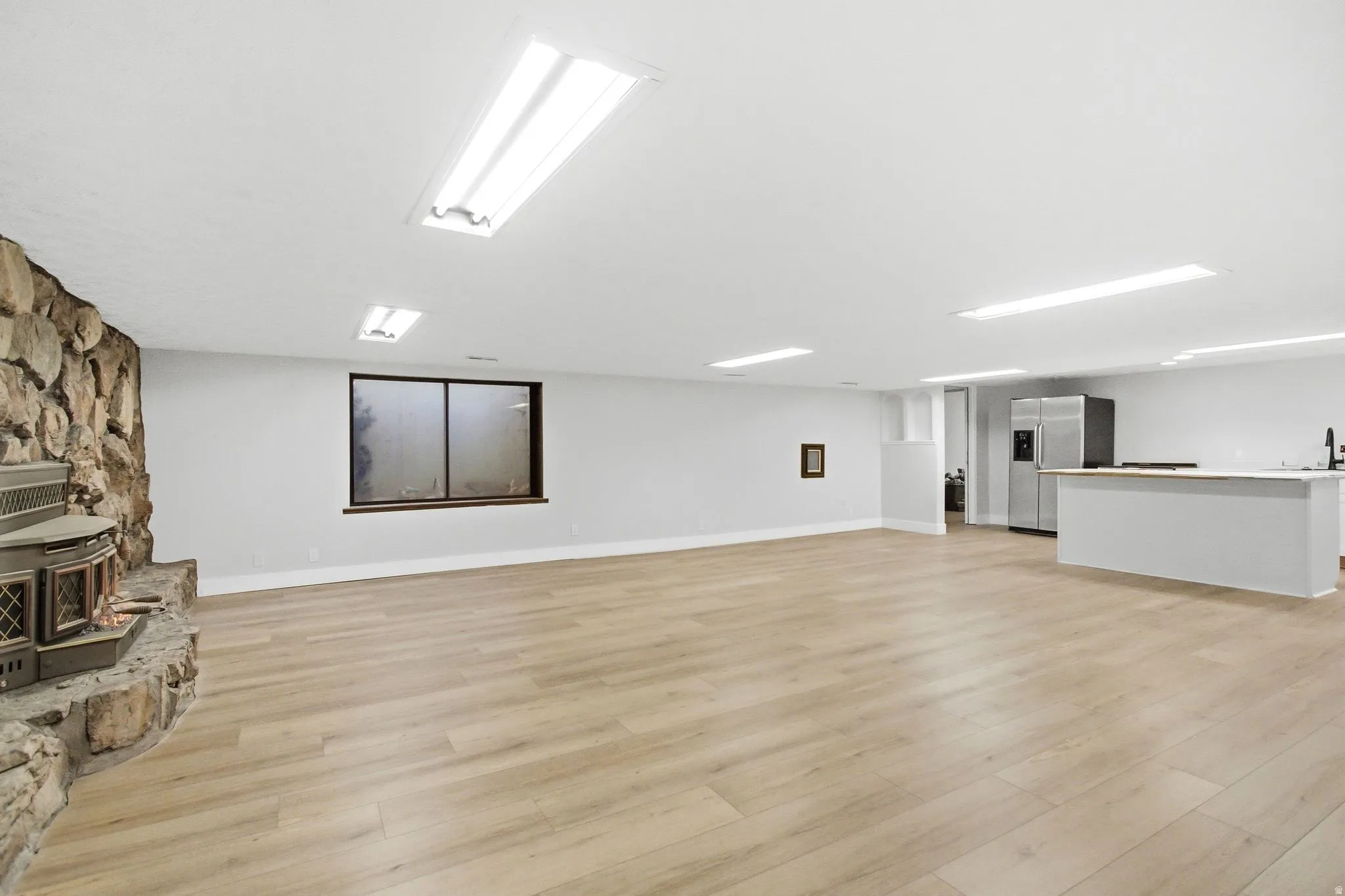 Open-concept recreation area featuring wood-finish flooring, a stone-clad fireplace, and recessed lighting