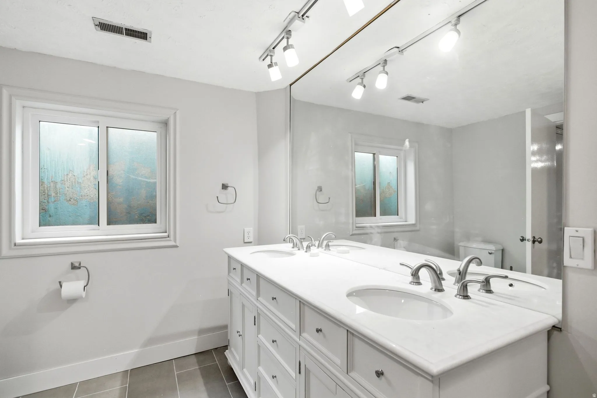 Bathroom featuring a double vanity with white cabinetry and integrated sinks, brushed nickel faucets, a large wall-mounted mirror, and tile flooring