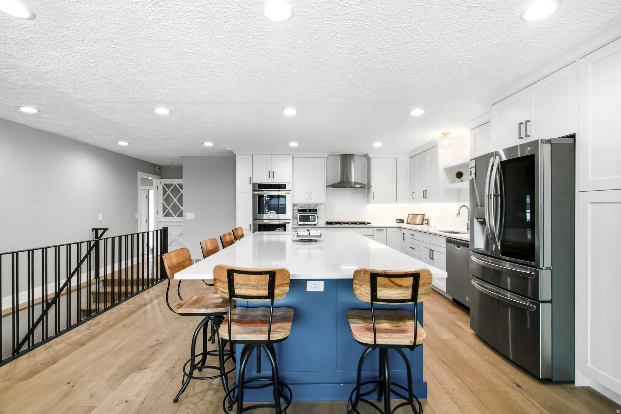 Open-concept kitchen featuring an expansive central island with a blue base, white quartz countertop, and seating for five