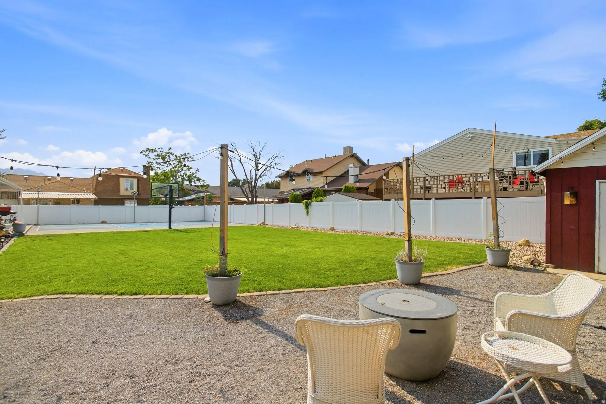 Expansive backyard featuring a gravel patio area with a built-in fire pit, a manicured lawn, a full-size sports court, and a red storage shed