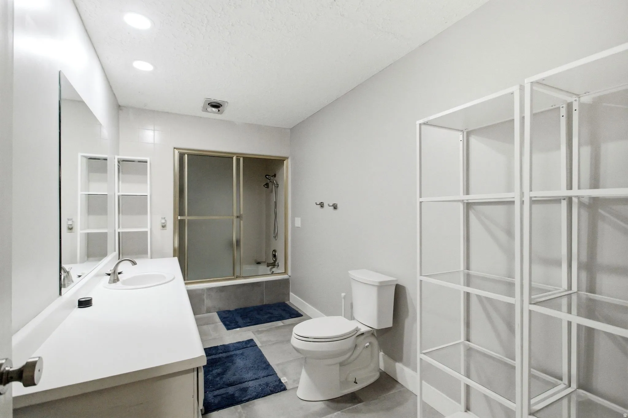 Bathroom featuring a single vanity with an integrated sink, large wall-mounted mirror, and recessed lighting