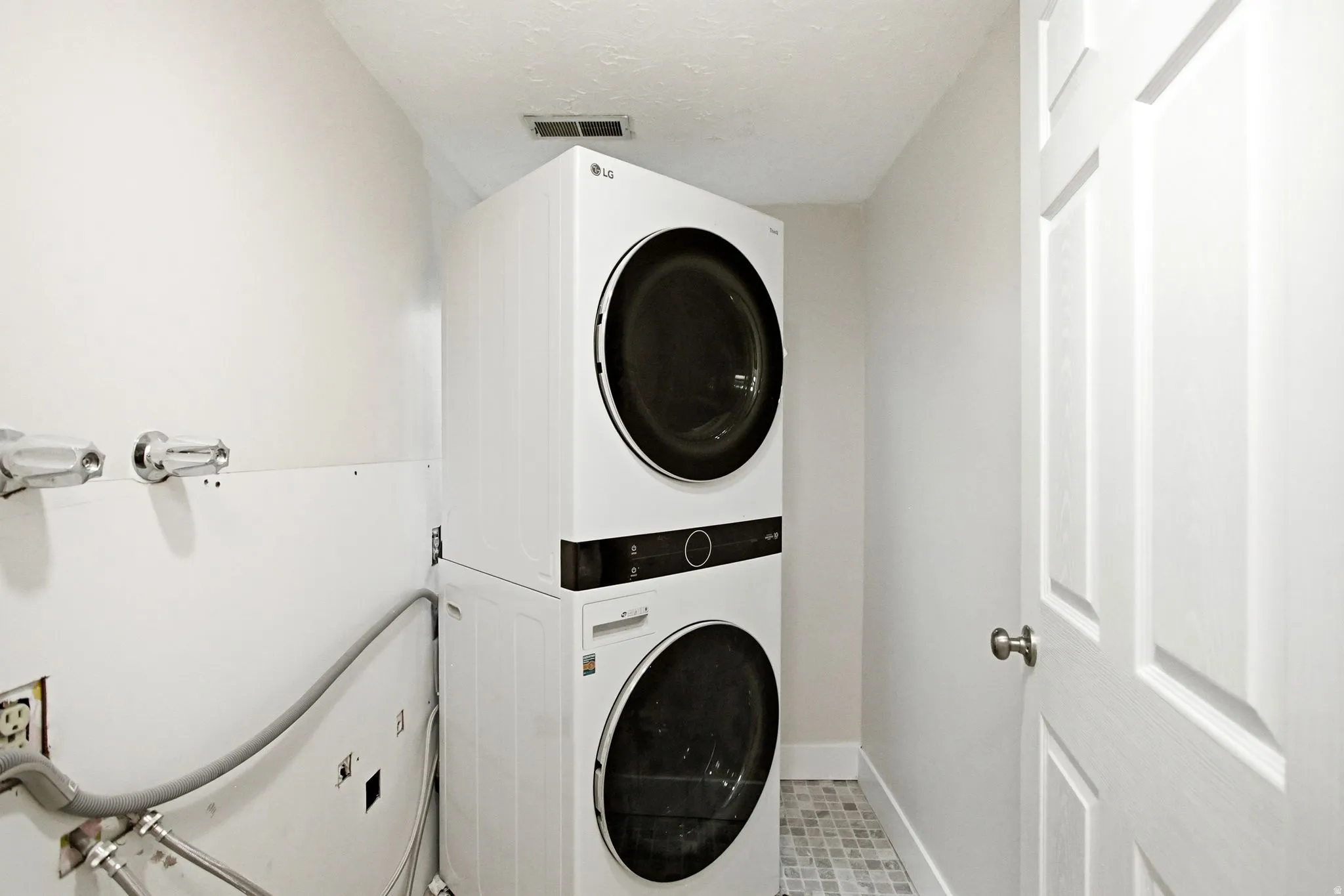 Compact laundry area featuring a stacked washer and dryer, tiled flooring, and a paneled interior door