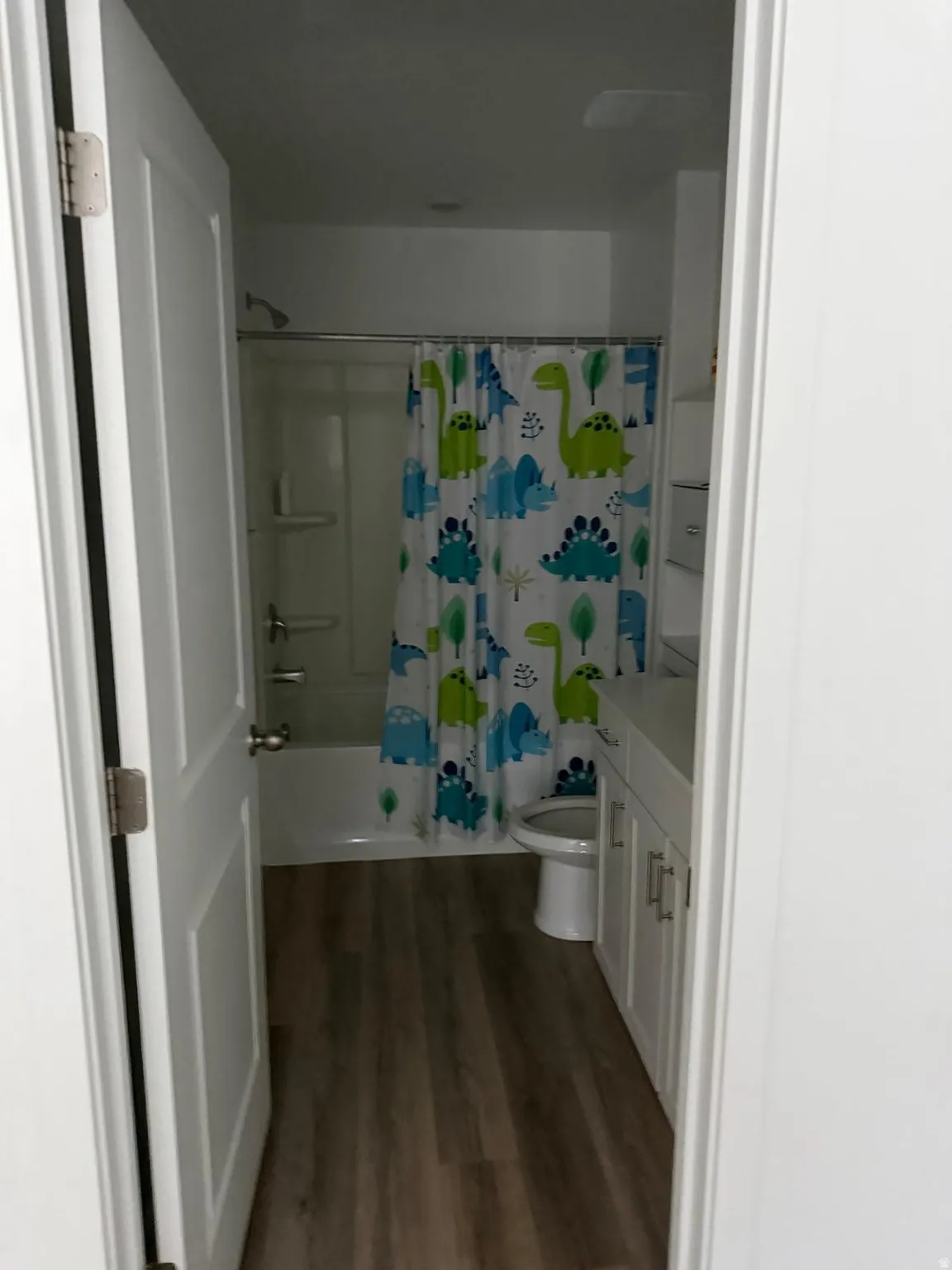 Full bathroom with wood-finish flooring, white vanity cabinetry, white countertop, and a white toilet