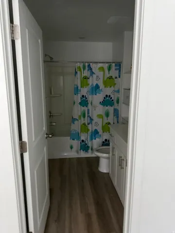 Full bathroom with wood-finish flooring, white vanity cabinetry, white countertop, and a white toilet