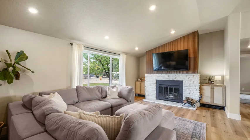 Living area featuring a stone-clad fireplace with a dark metal insert, a wood-slat accent wall, recessed lighting, and wood-finish flooring