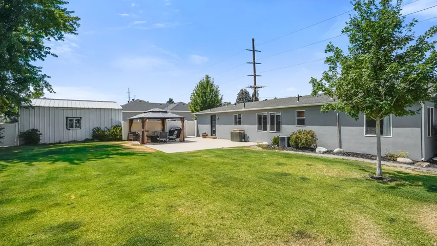 Expansive backyard featuring a large concrete patio, a freestanding gazebo, and a detached metal-sided outbuilding