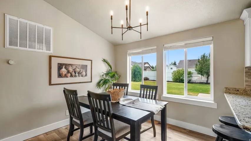 Dining area featuring wood-finish flooring, two large windows, a modern chandelier, and a vaulted ceiling