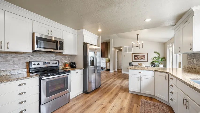 Kitchen featuring white cabinetry, stainless steel appliances, granite countertops, a mosaic tile backsplash, and wood-finish flooring