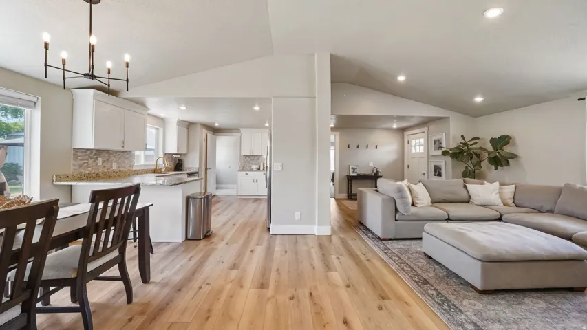 Open-concept living area featuring wood-finish flooring, vaulted ceilings, recessed lighting, and a modern chandelier