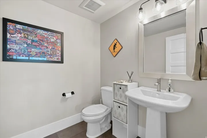 Pedestal sink with a brushed nickel faucet and a framed mirror, complemented by a two-bulb vanity light fixture