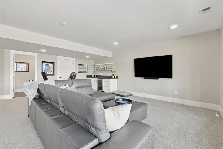 Spacious recreation room featuring recessed lighting, light-colored carpeting, and a built-in wet bar with white cabinetry and a dark countertop