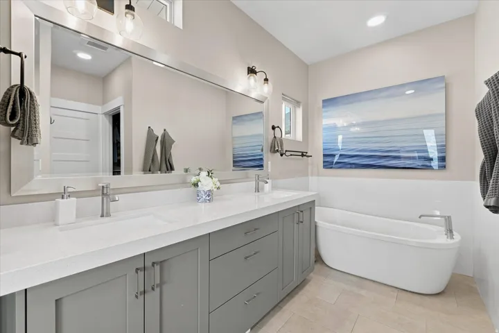 Spacious bathroom featuring a freestanding soaking tub, a dual vanity with a white countertop and gray cabinetry, and light wood-finish flooring