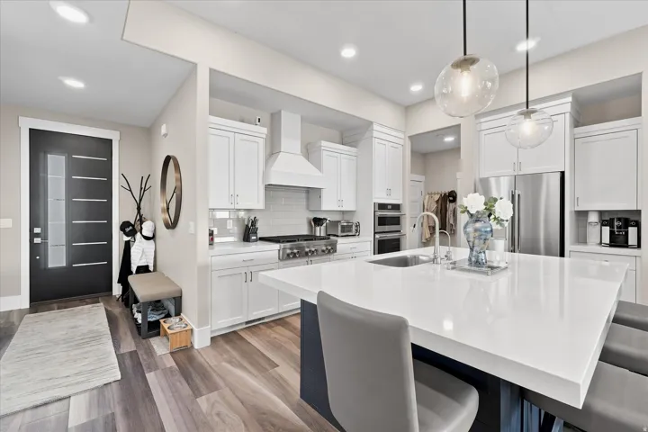 Open-concept kitchen featuring an expansive island with seating, white shaker cabinetry, stainless steel appliances, and wood-finish flooring