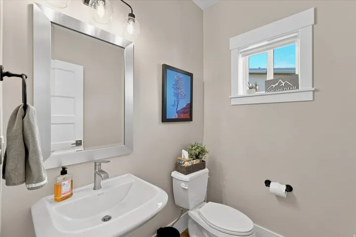 Powder room featuring a pedestal sink with a brushed nickel faucet, a framed mirror, and a wall-mounted light fixture with clear glass shades