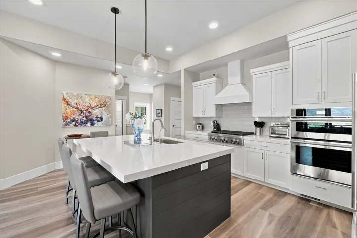 Modern kitchen featuring a large central island with a solid surface countertop, white shaker cabinetry, stainless steel appliances, and wood-finish flooring