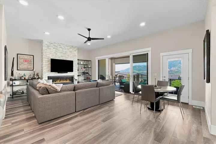 Open-concept living area featuring wood-finish flooring, a stacked stone fireplace surround, and recessed lighting