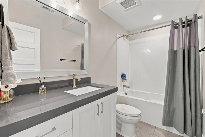 Modern bathroom featuring a single vanity with a sleek countertop, white cabinetry, undermount sink, and a framed mirror