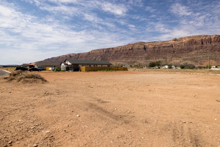 Expansive undeveloped lot featuring rugged terrain, a backdrop of natural rock formations, and a distant residential setting