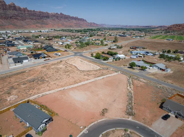 Expansive land parcel featuring clear ground, surrounded by established residential properties and roadways, with distant red rock formations