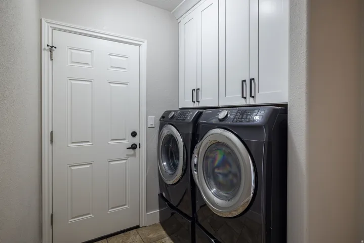 Laundry area featuring tile flooring, white shaker-style cabinetry with matte black hardware, and a white paneled door with matte black hardware