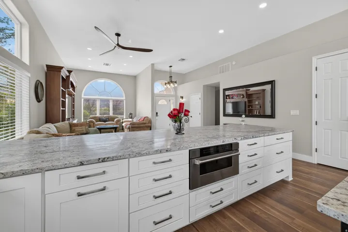 Spacious kitchen island featuring stone-finish countertops, white cabinetry with dark pulls, and a built-in stainless steel microwave drawer