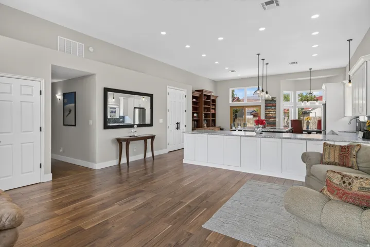 Open-concept kitchen and living area featuring wood-finish flooring, recessed lighting, white cabinetry, and granite countertops