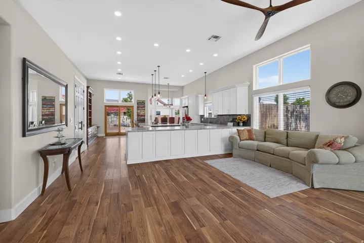 Spacious open-concept interior featuring wood-finish flooring throughout, a large kitchen island with a stone countertop, white shaker-style cabinetry, and high ceilings with recessed lighting