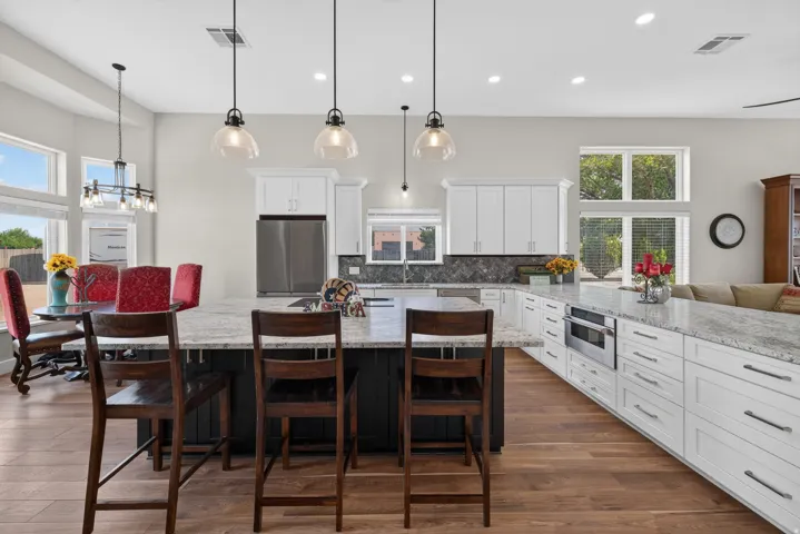 Spacious kitchen featuring an extended island with stone countertops, white cabinetry with dark hardware, stainless steel appliances, wood-finish flooring, and pendant lighting
