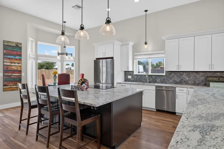 Contemporary kitchen featuring an expansive center island with seating, stainless steel appliances, white cabinetry, and wood-finish flooring