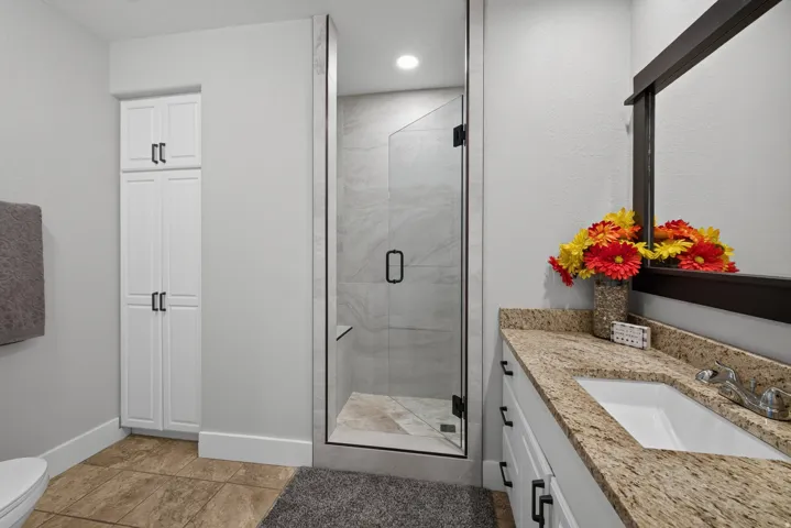 Bathroom featuring a glass-enclosed shower with tile surround, a single vanity with stone countertop, white cabinetry with dark hardware, and tile flooring