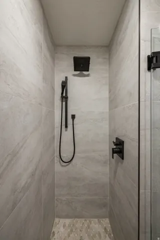 Shower enclosure featuring matte black fixtures, stone-look tile walls, and a decorative pebble-style tile floor
