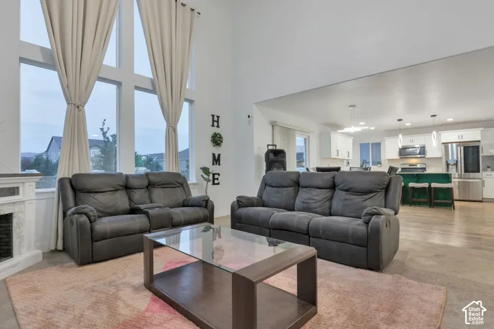 Two-story living room featuring expansive windows, high ceilings, a fireplace with a stone surround, and an open concept kitchen with stainless steel appliances and pendant lighting
