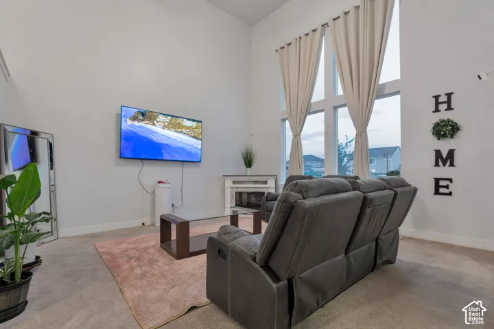 Spacious living area featuring a vaulted ceiling, floor-to-ceiling windows with drapes, and plush carpet flooring