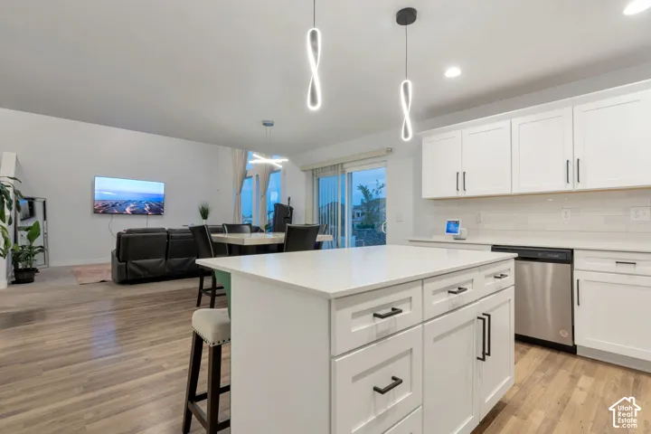 Modern kitchen featuring a white island with storage, white cabinetry, stainless steel dishwasher, and light-tone wood-finish flooring