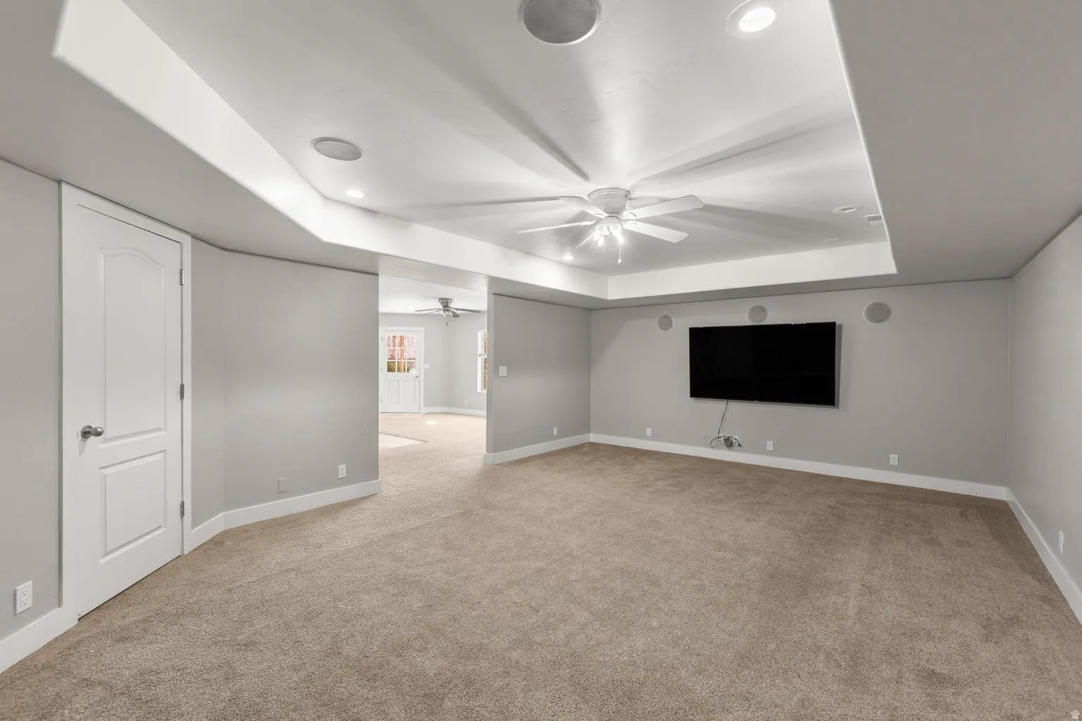 Spacious interior room featuring a tray ceiling with recessed lighting and a ceiling fan
