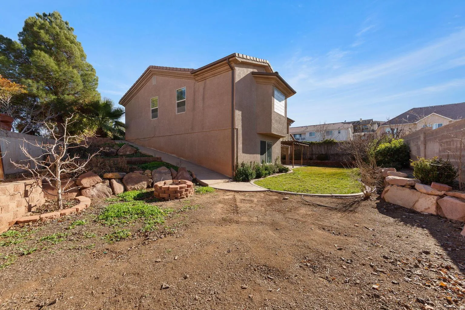 Rear exterior featuring an upper-level bay window, a lower-level patio with a pergola, and a manicured lawn area