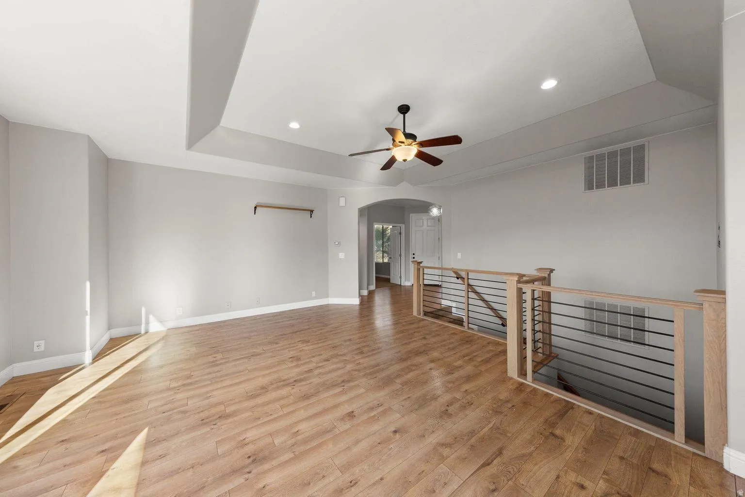 Spacious room featuring wood-finish flooring, a tray ceiling, recessed lighting, and a ceiling fan