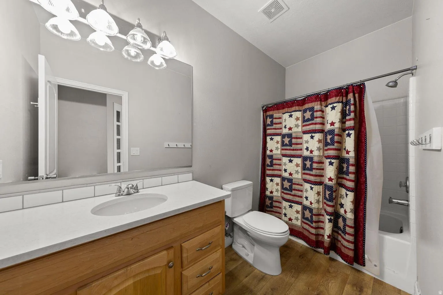 Bathroom featuring a wood-finish vanity with a white countertop and integrated sink, a large wall mirror, and a full-size bathtub with a shower fixture