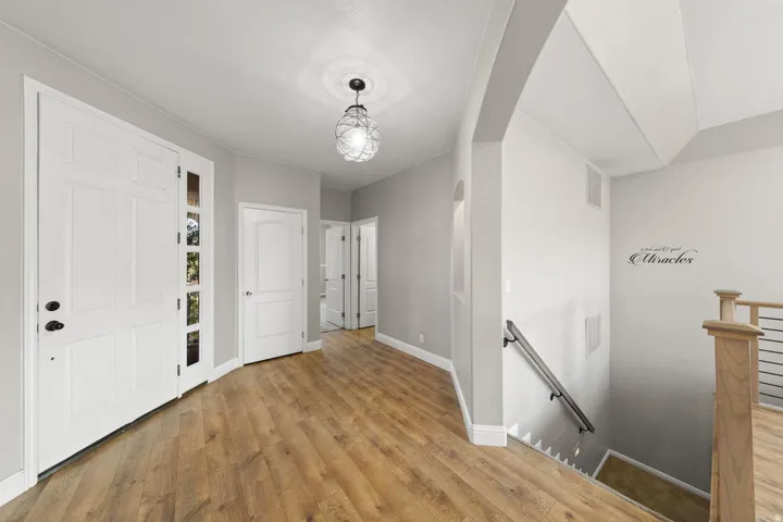 Entryway featuring wood-finish flooring, a contemporary ceiling light fixture, a paneled entry door with sidelights, and a staircase with a wood newel post and metal balusters