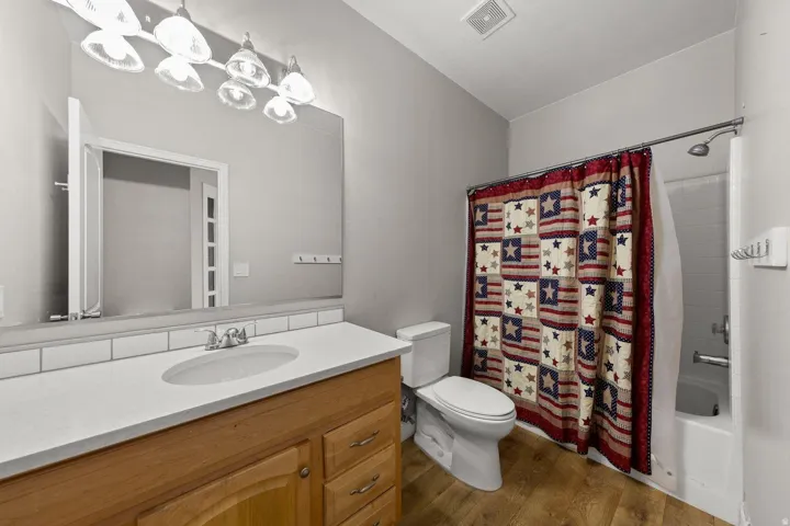 Bathroom featuring a wood-finish vanity with a white countertop and integrated sink, a large wall mirror, and a full-size bathtub with a shower fixture
