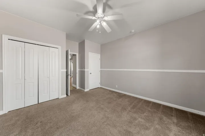 Neutral-toned room featuring a vaulted ceiling with a white ceiling fan