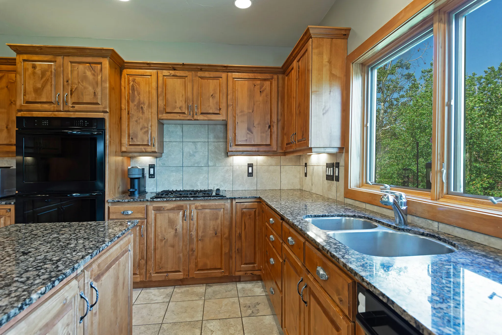 Kitchen featuring wood cabinetry, stone countertops, a tile backsplash, and a double basin sink