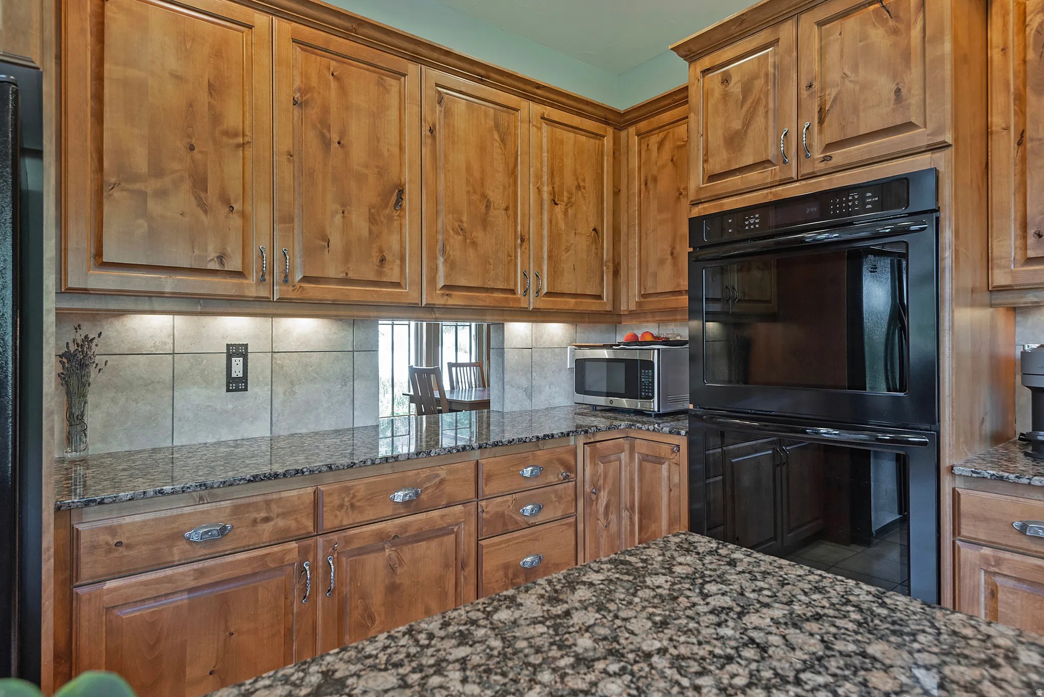 Built-in double oven within a kitchen featuring wood cabinetry, granite countertops, and a tiled backsplash