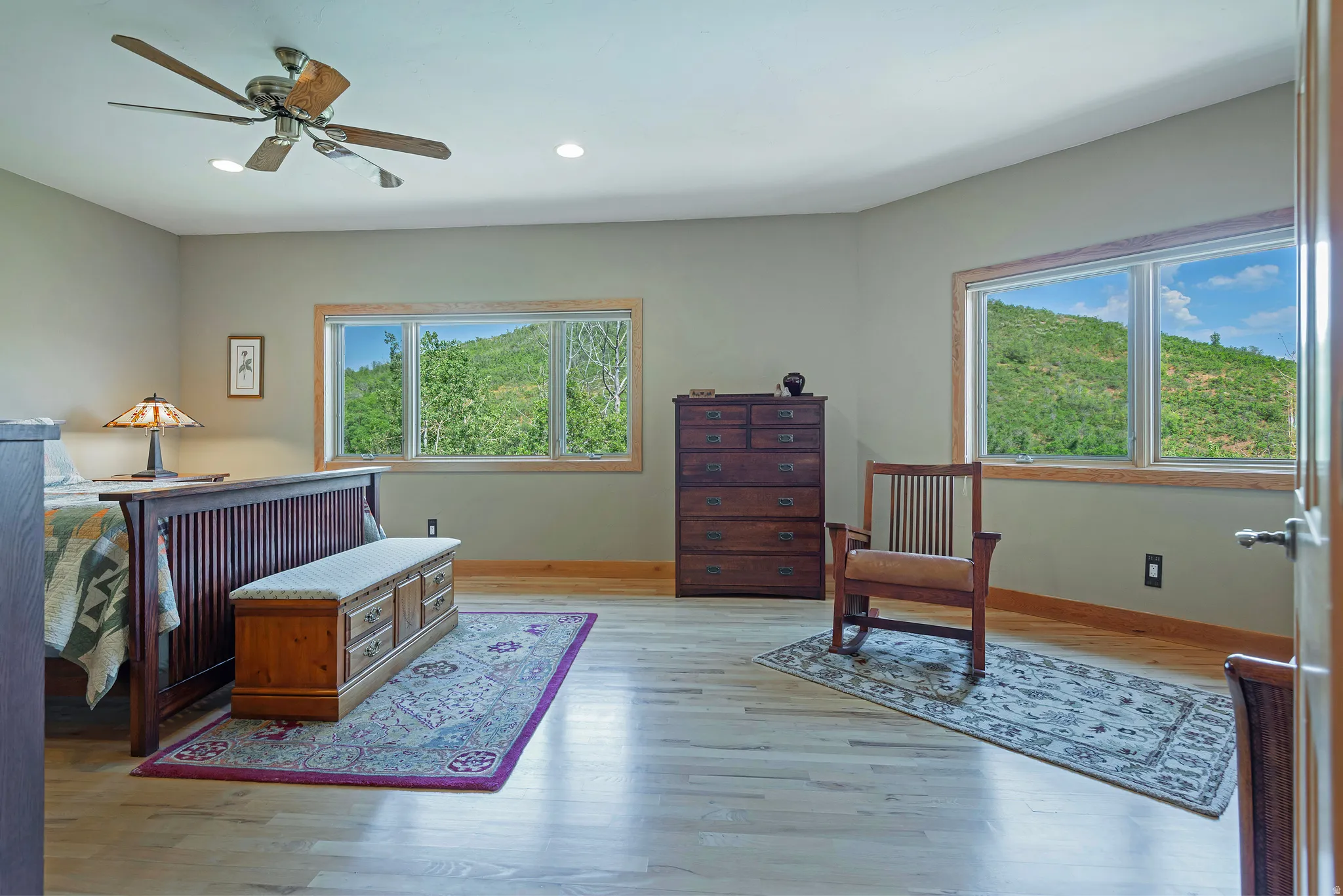 Spacious room with light wood-finish flooring, two large windows with natural wood trim, and a ceiling fan with integrated lighting