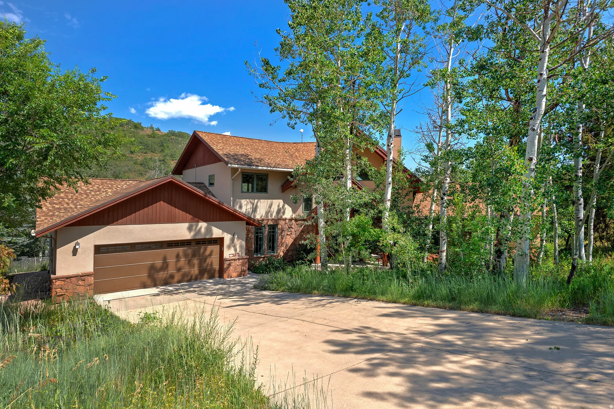 Multi-level residence featuring a two-car garage with a brown panel door, stone base detailing, and stucco siding